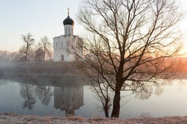 A misty lake with a boat in front of the church in the early spring at dawn clipart