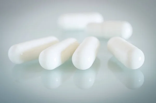 Witte medische capsules liggen op het spiegelend oppervlak — Stockfoto