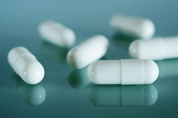 White medical capsules lie on the mirror surface — Stock Photo, Image