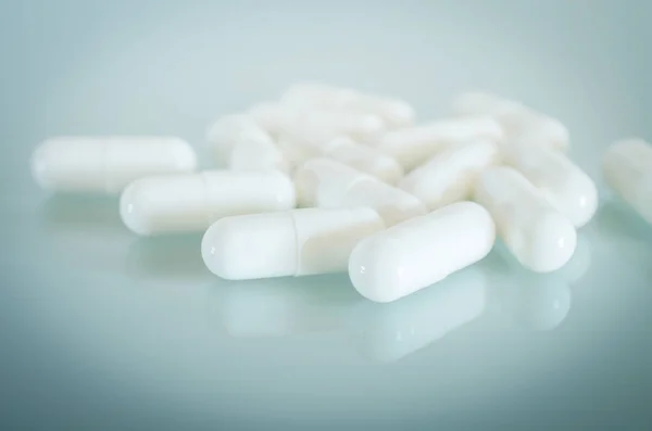 Witte medische capsules liggen op het spiegelend oppervlak — Stockfoto