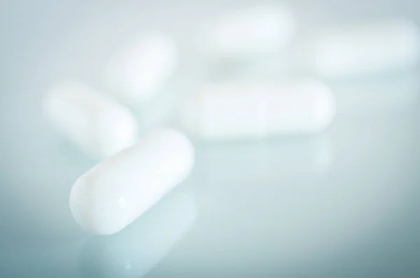 White medical capsules lie on the mirror surface — Stock Photo, Image