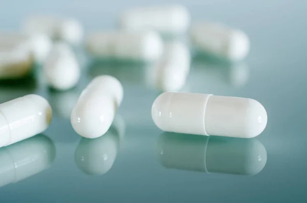 White medical capsules lie on the mirror surface — Stock Photo, Image