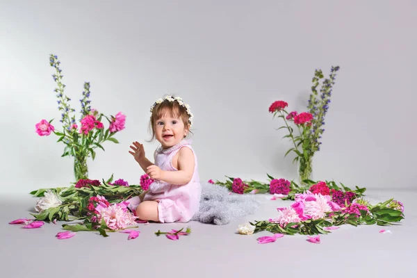 Feliz un niño pequeño se sienta con una flor, fondo gris . — Foto de Stock
