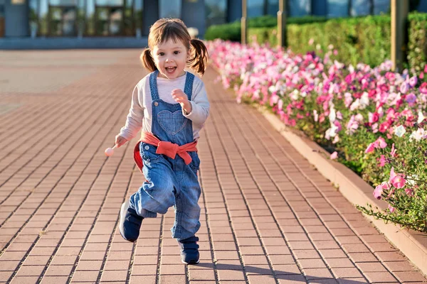 Legrační malá dívka, která skočila pro joy.little dívku v džínová kombinéza. — Stock fotografie