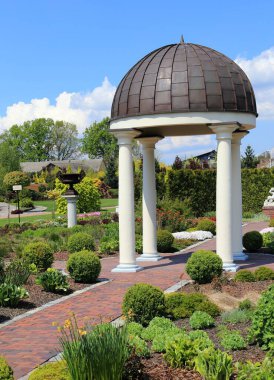 Baharda renkli bir bahçe manzarası, bitkiler ve ağaçlar için çeşitli yeşil tonlarda. Bahçe çardağı.