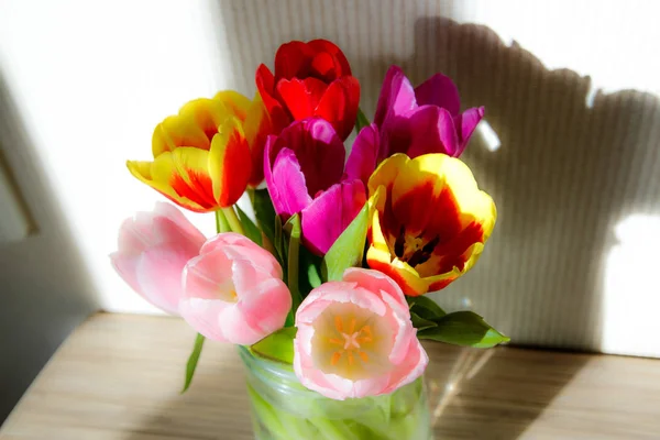 A bouquet of tulips in the sun is on a table in a vase — Stock Photo, Image