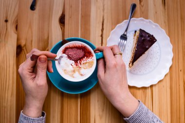 Eller şeker bir fincan kahve pasta yanındaki ahşap bir masa üzerinde karıştırma