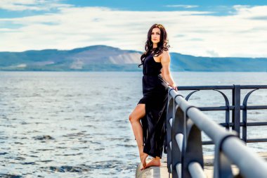 Genç ve güzel bir kız su ve dağların arkasında duruyor.