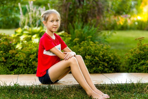 Dziewczyna siedzi na ścieżce w ogrodzie — Zdjęcie stockowe