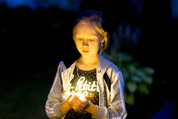 A menina segura as luzes à noite no jardim — Fotografia de Stock