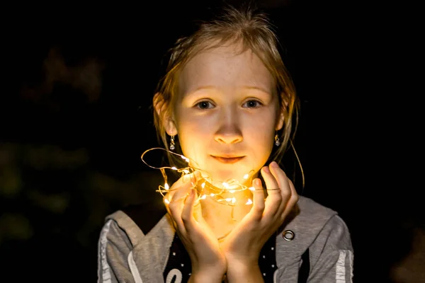 A menina segura as luzes à noite no jardim — Fotografia de Stock