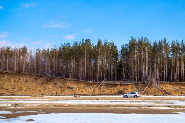 Beyaz araba baharda kumlu bir plaj üzerinde bir uçurum ve orman ve mavi gökyüzü bir arka plan üzerinde duruyor