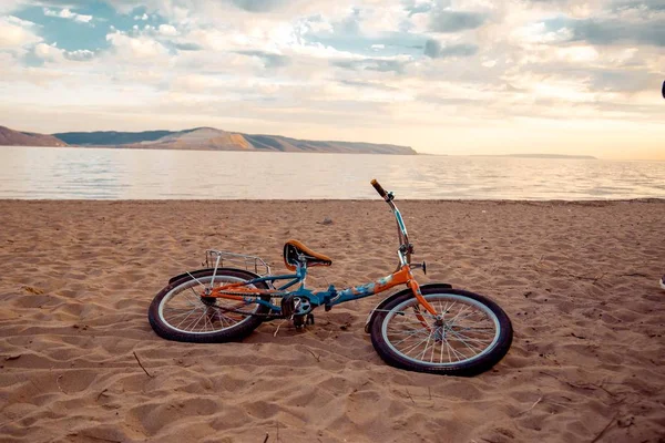 Un vélo repose sur le sable sur la rive de la rivière — Photo