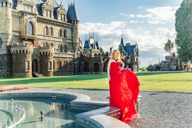 Kırmızı elbiseli bir kadın, Haziran 2019 'da Togliatti' de bir ortaçağ şatosunun arka planında duruyor.