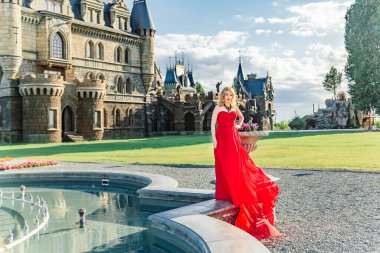 Kırmızı elbiseli bir kadın, Haziran 2019 'da Togliatti' de bir ortaçağ şatosunun arka planında duruyor.