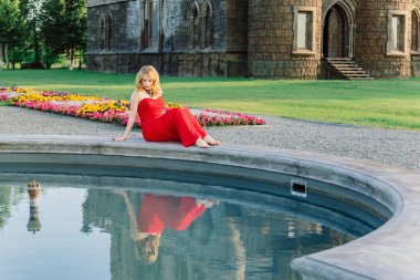 Kırmızı elbiseli bir kadın ortaçağ şatosunun arka planında duruyor.