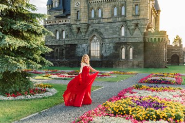 Kırmızı elbiseli bir kadın, Haziran 2019 'da Togliatti' de bir ortaçağ şatosunun arka planında duruyor.