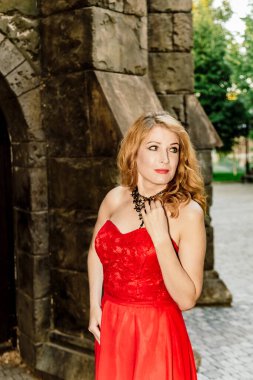 Kırmızı elbiseli bir kadın ortaçağ şatosunun arka planında duruyor.