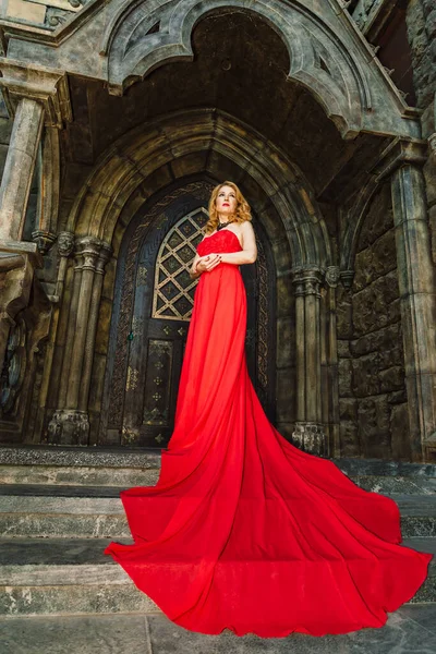 stock image A woman in a red dress stands on a background of a medieval castle