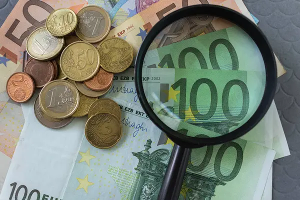 Увеличительное стекло на куче банкнот и монет евро как бизнес — стоковое фото
