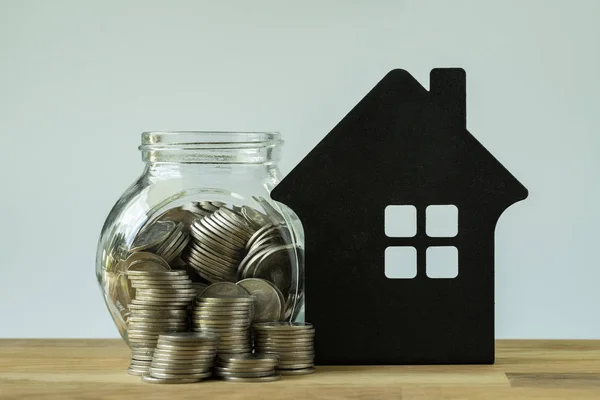 Stapel van munten en munten in glazen pot met papier huis op houten — Stockfoto