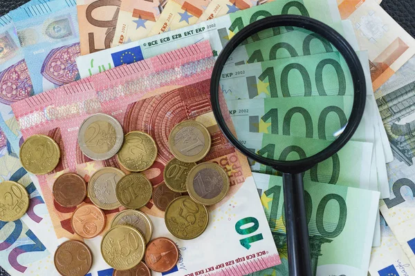 Увеличительное стекло на стопке банкнот евро с монетами евро — стоковое фото