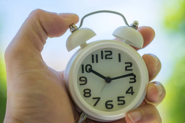 Mano de la mujer sosteniendo un reloj despertador blanco como cupón de negocios o tiempo — Foto de Stock