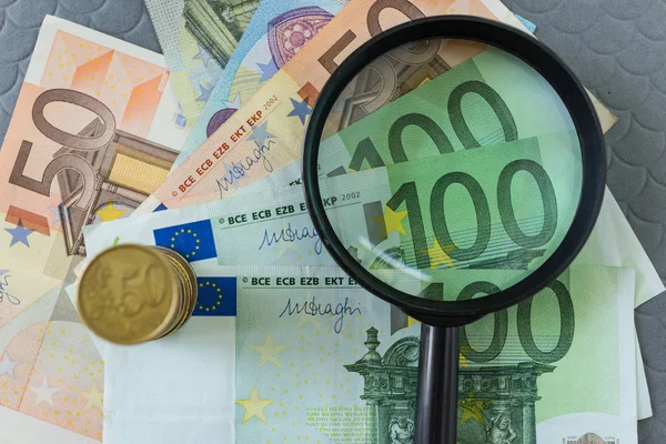 Lupa sobre pila de billetes y monedas en euros como negocio — Foto de Stock