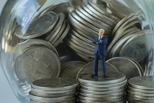 Hombre de negocios en miniatura de pie en la pila de monedas como su financiera — Foto de Stock