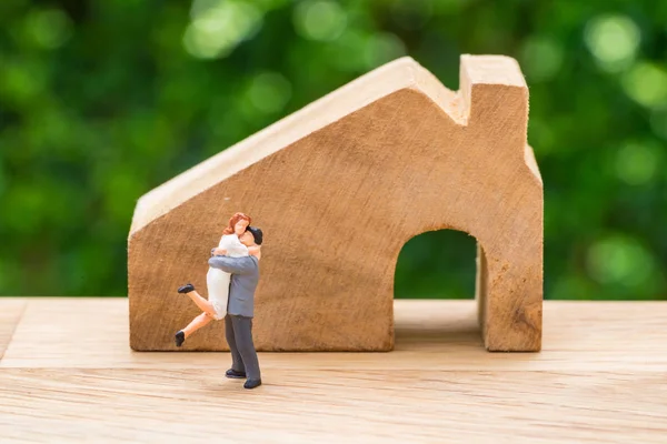 Miniatura feliz pareja familia de pie con casa de madera como apoyo — Foto de Stock