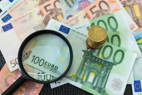 Пачка монет евро на пачке банкнот с лупой — стоковое фото