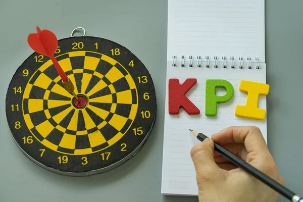 Tangan memegang pensil dan alfabet KPI warna-warni dengan dartboard sebagai — Stok Foto