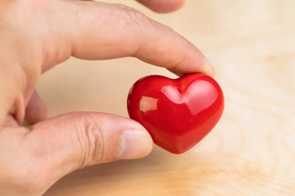 Main tenant en forme de coeur rouge avec les doigts sur fond en bois u — Photo