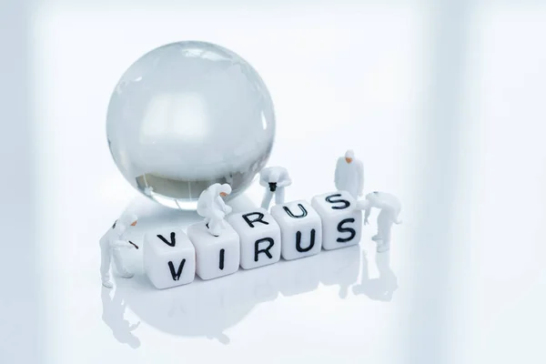 World wide spreading or coronavirus, COV, COVID-19 flu outbreak concept, miniature people doctors with protective suit inspecting cube block combine the word Virus with world globe glass ball.