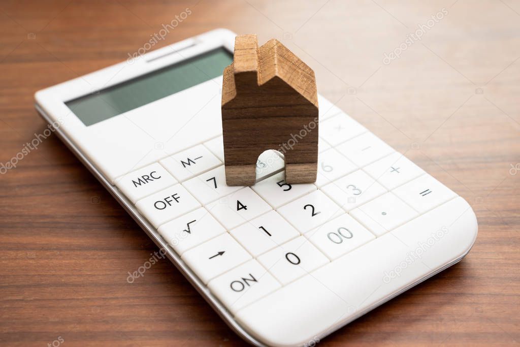 Mortgage calculation, buy and sell house or real estate or cost and expense for house owner concept, small wooden house on white calculator on wooden table.