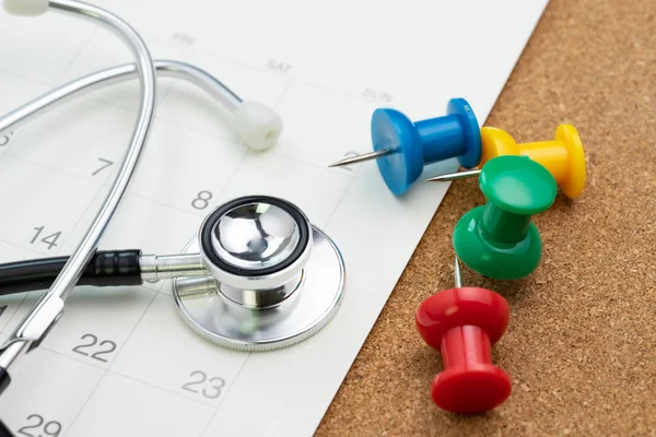 Schedule or appointment for medical exam or meet the doctor for health check up concept, colorful thumbtack or pushpin with white calendar and doctor stethoscope.