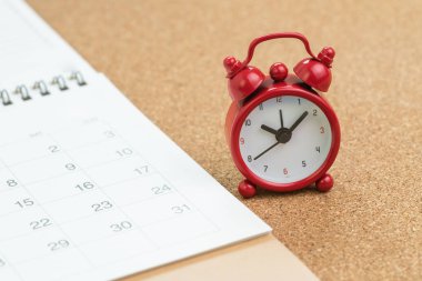 Ahşap masa arkasında beyaz takvimli kırmızı alarm saati, tatil programı, iş randevusu için hatırlatma veya iş projesi için son tarih.