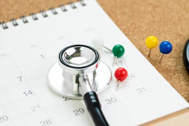 Renkli raptiyeli steteskop ya da beyaz takvimde raptiye, takvim ya da sağlık muayenesi için randevu ya da sağlık kontrolü konsepti için doktorla görüşmek.