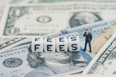 Ücretler, iş konsepti için ödenen hizmetler veya finansal harcamalar, takım elbiseli minyatür işadamı, küp blokla ABD doları para banknotları üzerine harç inşa etmeyi düşünüyor.