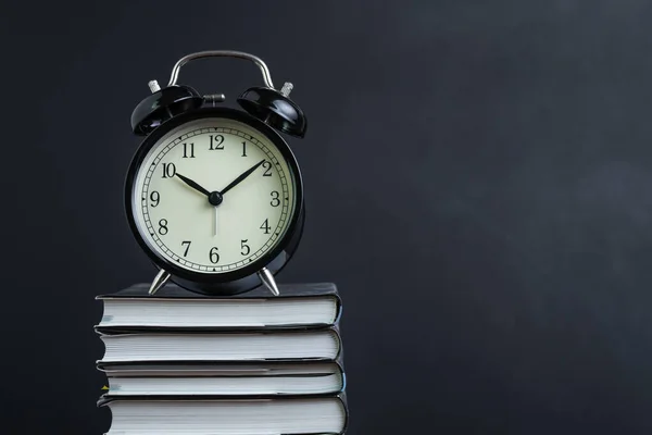 Alarm clock on stack of textbook with chalkboard or blackboard background copy space, time for reading, concentration in study, homework or educational concept.
