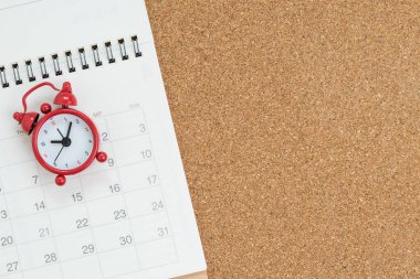 Ahşap masa arkasında beyaz takvim bulunan kırmızı alarmlı saatin düz görünümü veya üst görünümü, tatil çizelgesi, iş randevusu için hatırlatma veya iş projesi için son tarih.