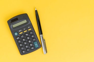 Fotokopi alanı, matematik, maliyet, vergi veya yatırım hesaplamaları boş olan açık sarı arkaplan tablosu üzerinde hesap makinesi olan siyah kalemin düz görünümü.