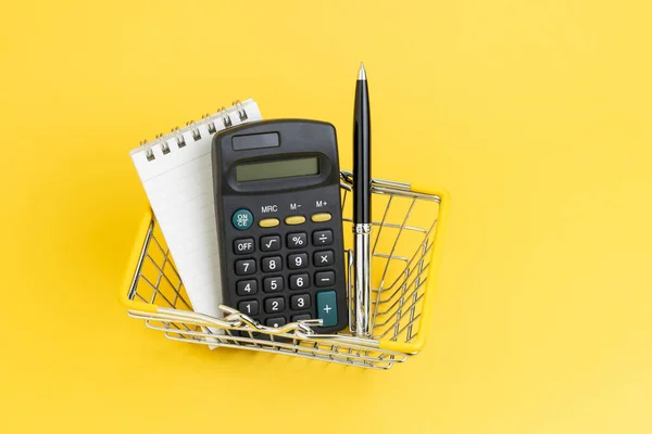 带有记事本清单和钢笔的计算器 装在黄色背景的迷你购物篮中 购物单 以最小价格或超级市场概念购买物品的成本和费用 — 图库照片