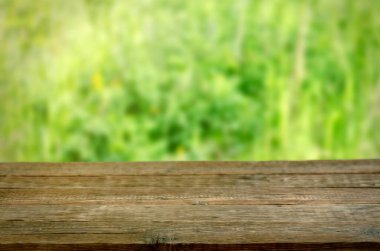 Yeşil çimenli bahar arka planı ve doğal bir bokeh arka planda boş bir tahta masa. Ürünlerinizi görüntülemek veya montajlamak için kullanılabilir.