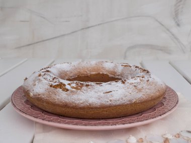 Ciambellone pembe seramik plaka üzerinde pudra şekeri serpilir.