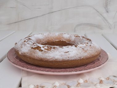 Ciambellone pembe seramik plaka üzerinde pudra şekeri serpilir.
