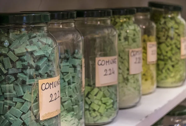 glass jars on a shelf containing colored glass and ceramic bits