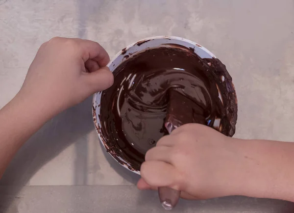 Manos de un niño juegan el chef pastelero mezclando chocolate en un tazón —  Fotos de Stock