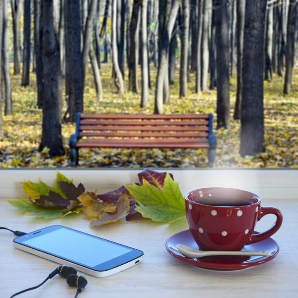 窓辺に一杯のコーヒー、スマート フォン、ヘッドフォンと秋を残します。秋の風景と背景のウィンドウで — ストック写真