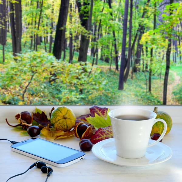 一杯のコーヒー、スマート フォンとヘッドフォン、秋の葉、カボチャや栗、窓辺に。秋の風景と背景のウィンドウで — ストック写真